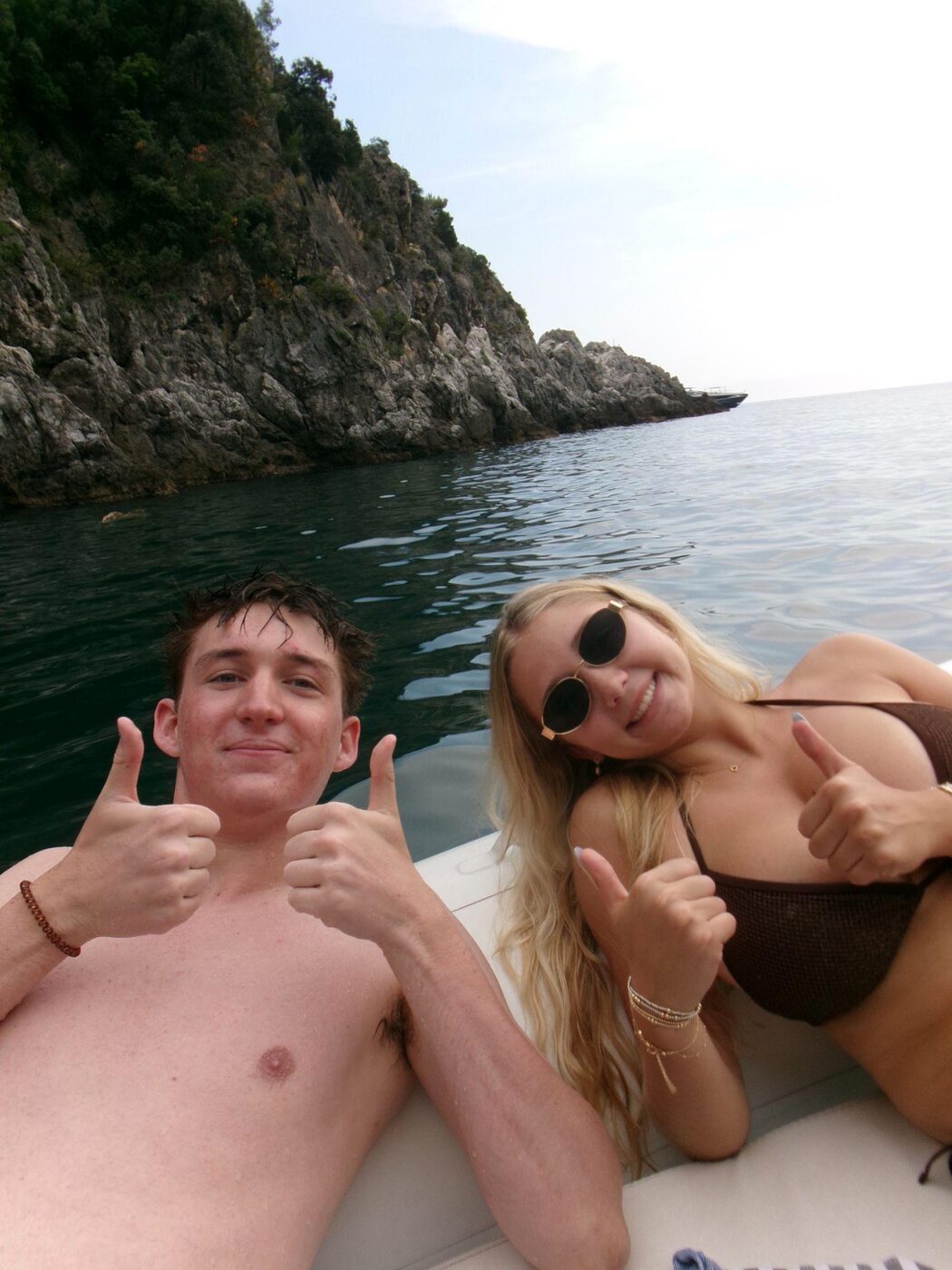 Two thumbs up on the boat by the rocky coastline