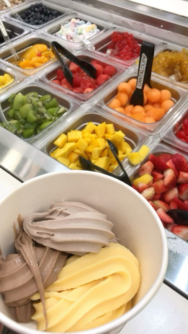 A cup of frozen yogurt in front of the toppings bar