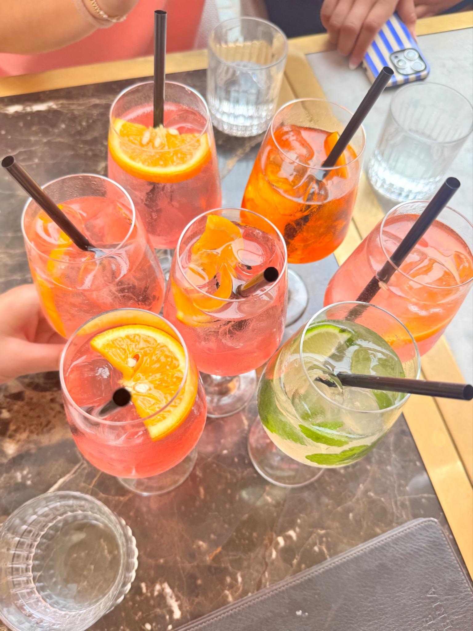 A table of orange and pink spritzes with straws