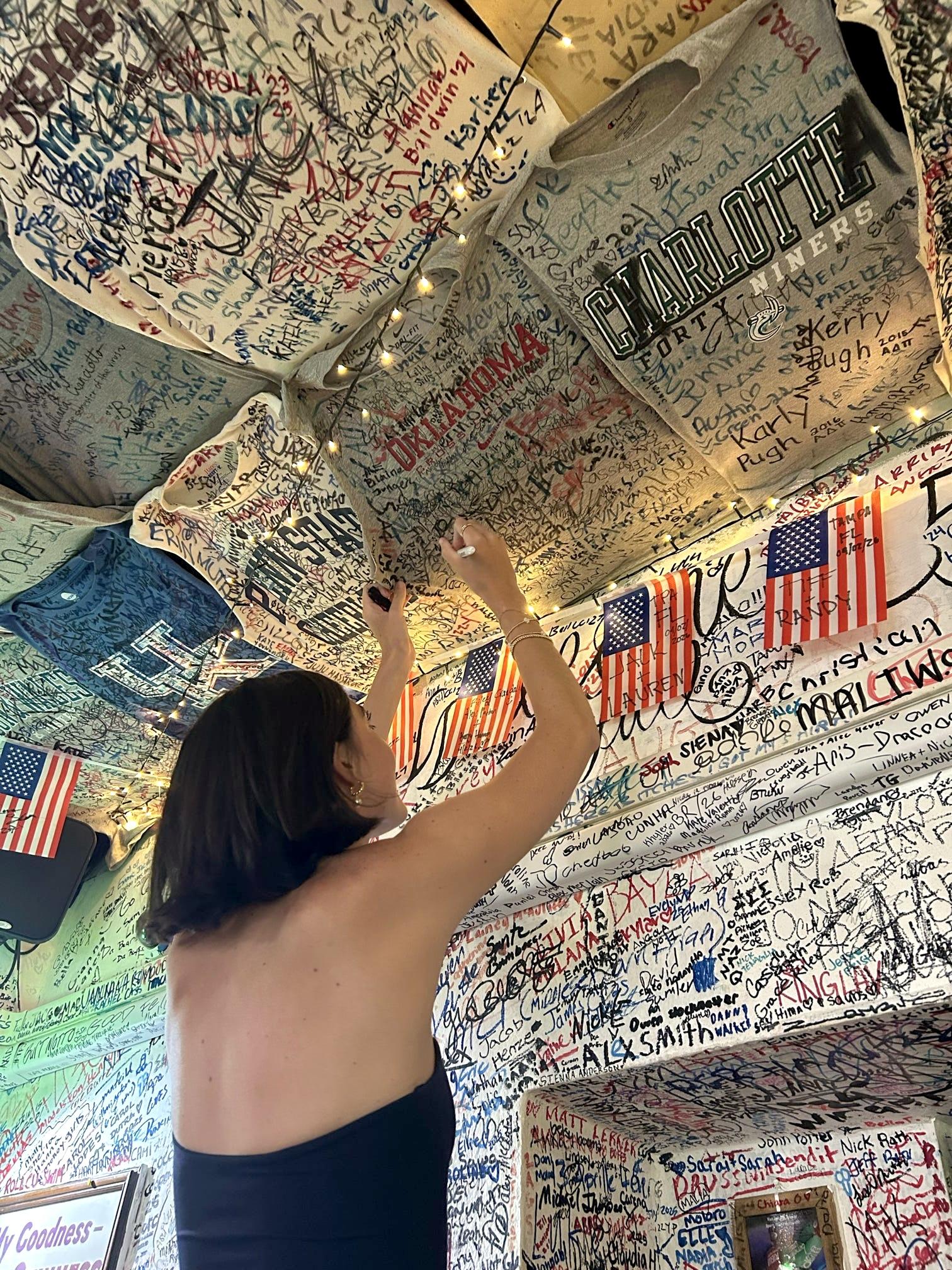 Reaching up to sign the OU shirt among the t-shirts covering the ceiling at Lions Fountain